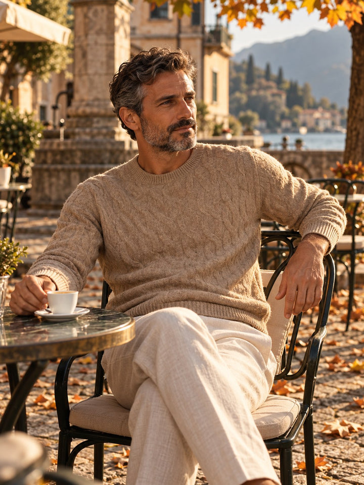 Man in a beige cashmere cable crewneck at a lakeside cafe in autumn